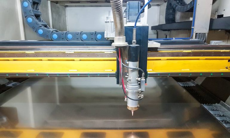 A laser machine working with a piece of metal. The laser machine is getting ready to dispense plasma surface treatment.