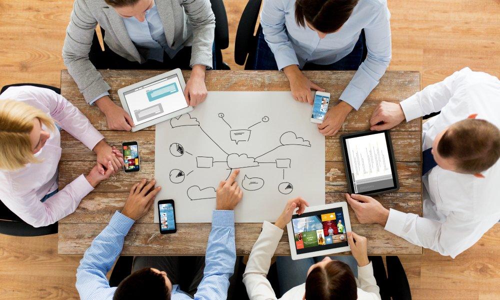 A business marketing team sitting around a table on devices as they plan a social media content strategy.