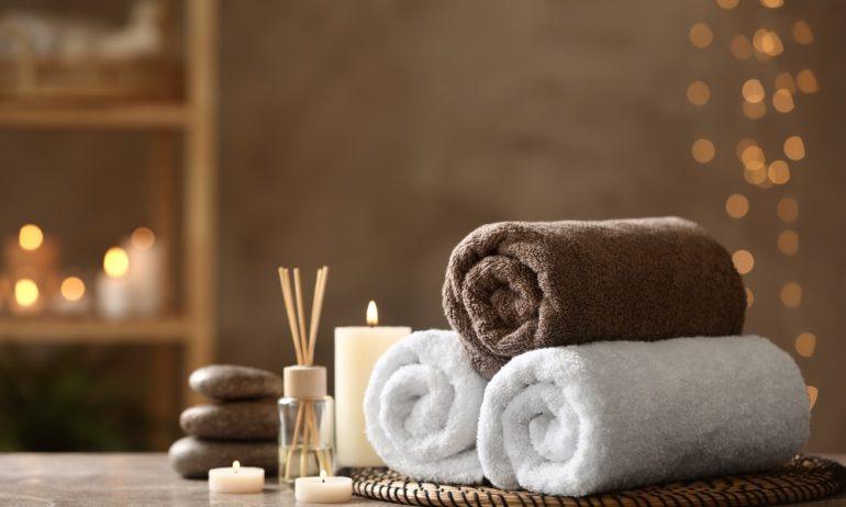 A wellness spa with ambient lighting and a gray stone table with rolled towels, tealights, and an oil diffuser.